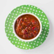 Top down view of a green and white polka dot plate, on which sits a bowl with bright red slivers of roasted red peppers in a pomegranate molasses dressing