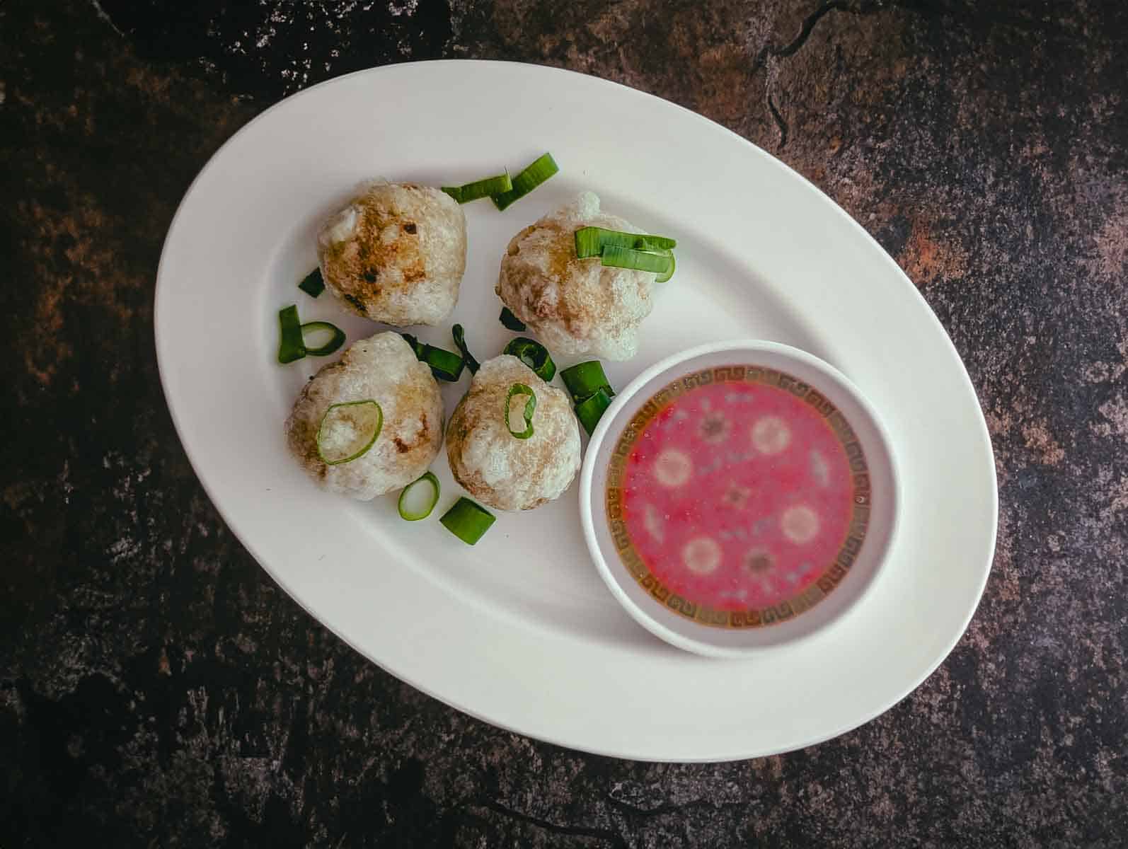 Four balls with icy-white coating from deep frying, on a white oval dish alongside clear dipping sauce