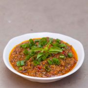 White bowl with red/orange coconut and mushroom relish, topped with flecks of green spring onions