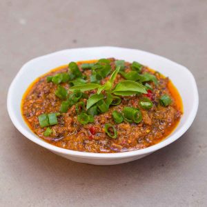 White bowl with oil red relish, topped with flecks of green spring onion