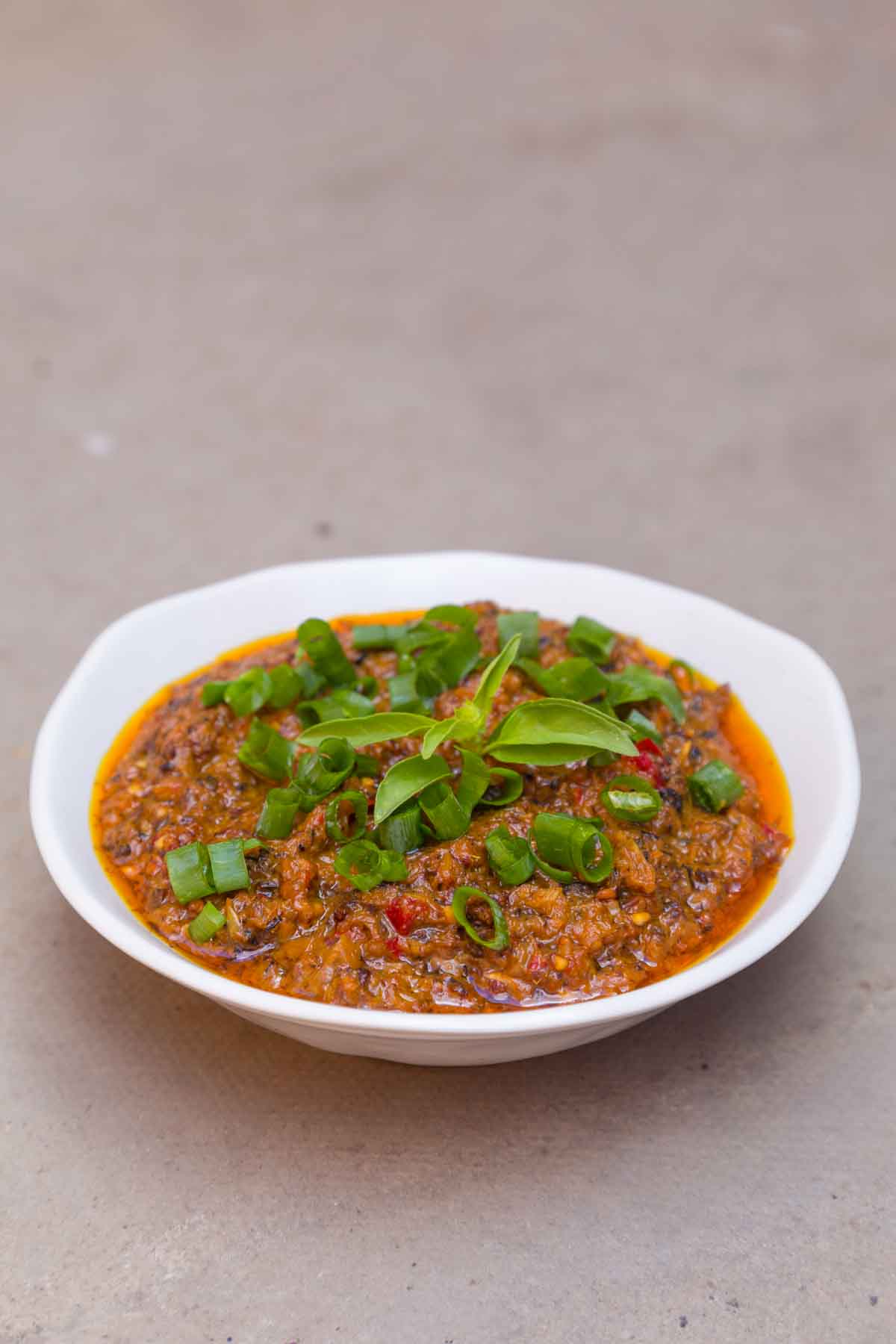 White bowl with red/orange coconut and mushroom relish, topped with flecks of green spring onions