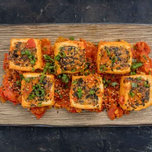 Top down view of 6 pieces of lemongrass stuffed tofu on a brown rectangular plate