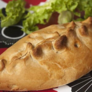 vegan baked bean and cheese pasty on a patterned red and black plate with some lettuce