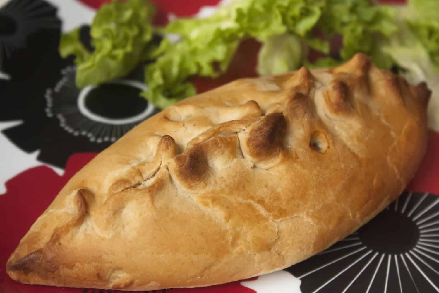 vegan baked bean and cheese pasty on a patterned red and black plate with some lettuce