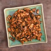 top down view of kering tempe. A blueish green square plate piled with shiny deep fried tempeh and peanuts