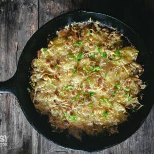 top down view of a large black cast iron skillet filled with a crispy-cheesy topped potatoe and onion casserole.