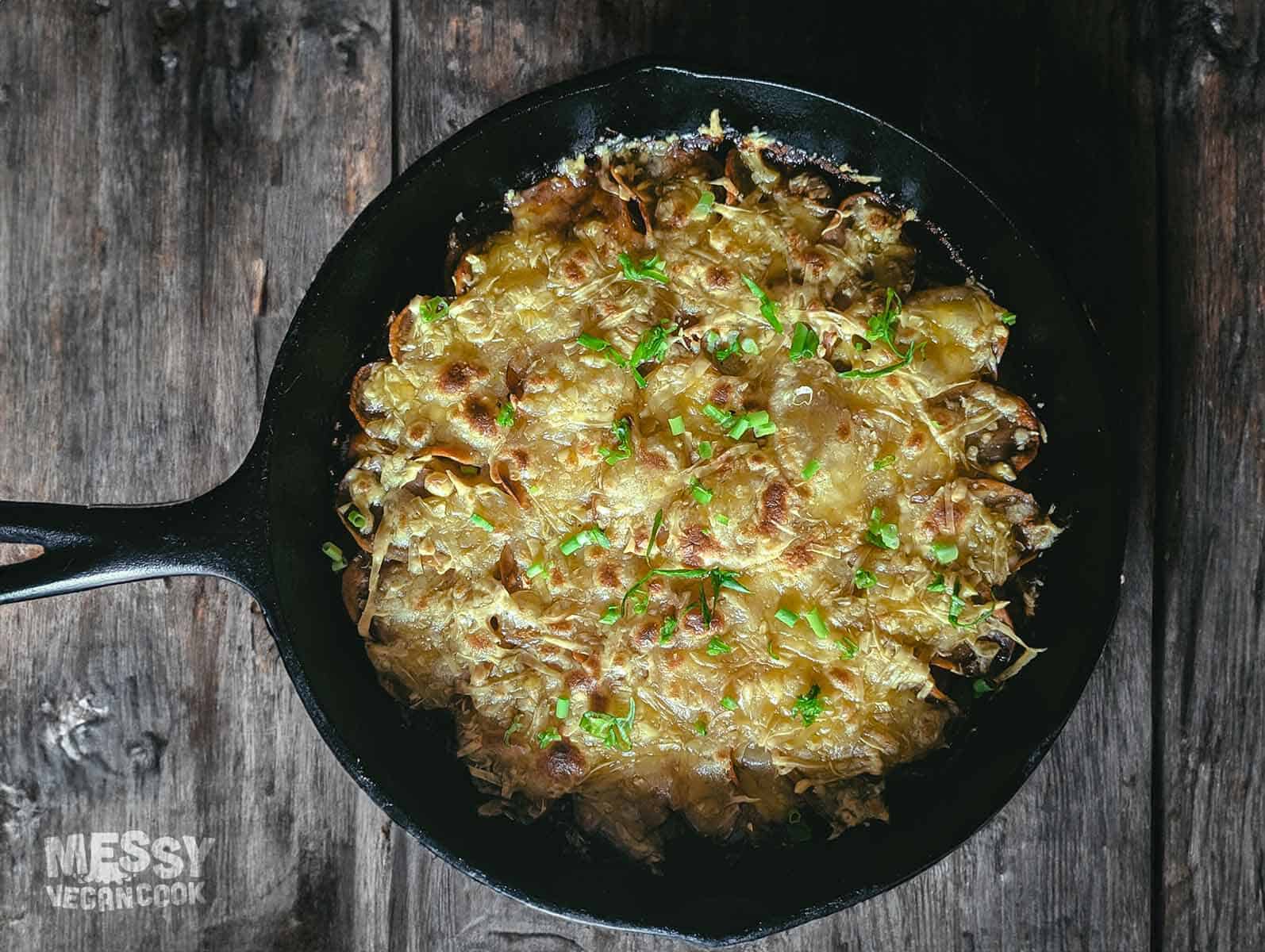 top down view of a large black cast iron skillet filled with a crispy-cheesy topped potatoe and onion casserole.