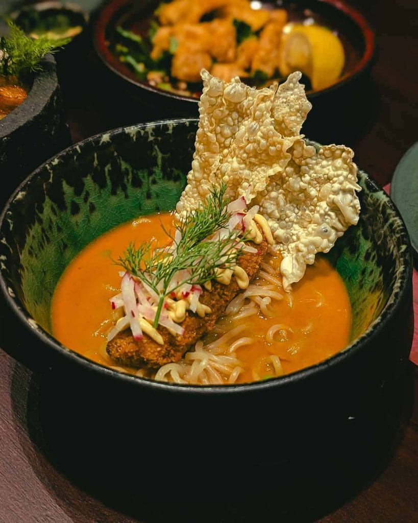 Dark black and green bowl filled halfway with orang coloured curry, with some noodles visible in the soup