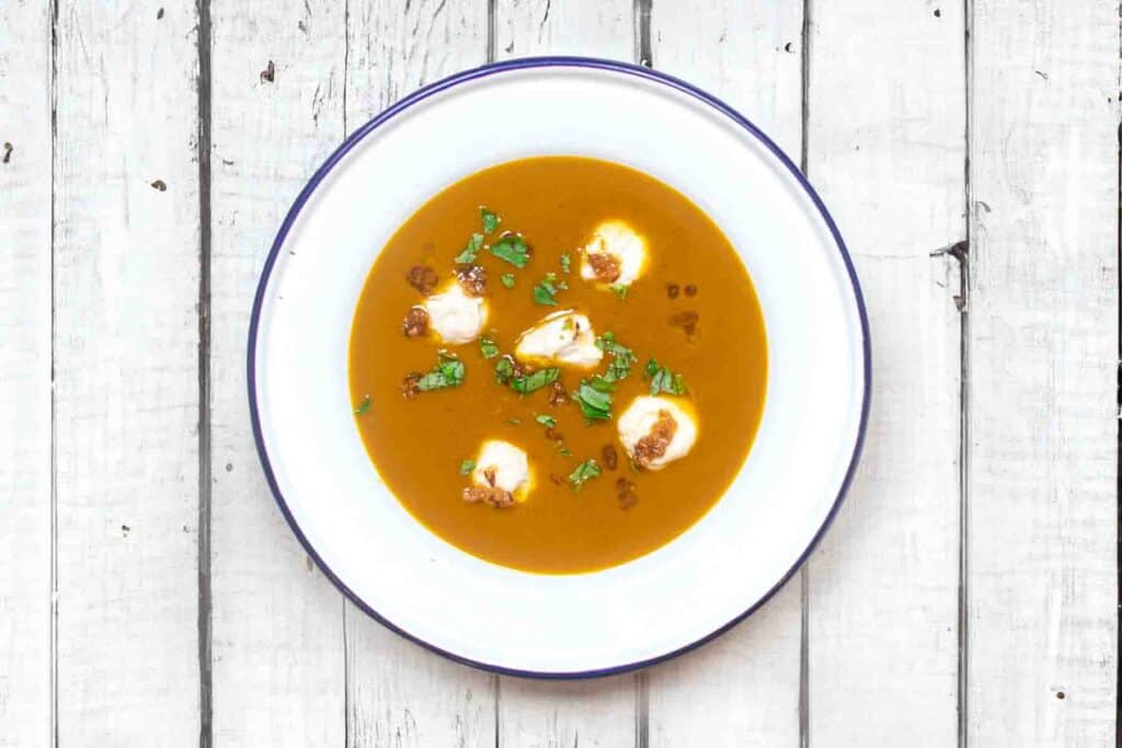 overhead shot of pumpkin and sweet potato soup with five evenly space white blobs (peanut dumplings) and some parsley for contrast