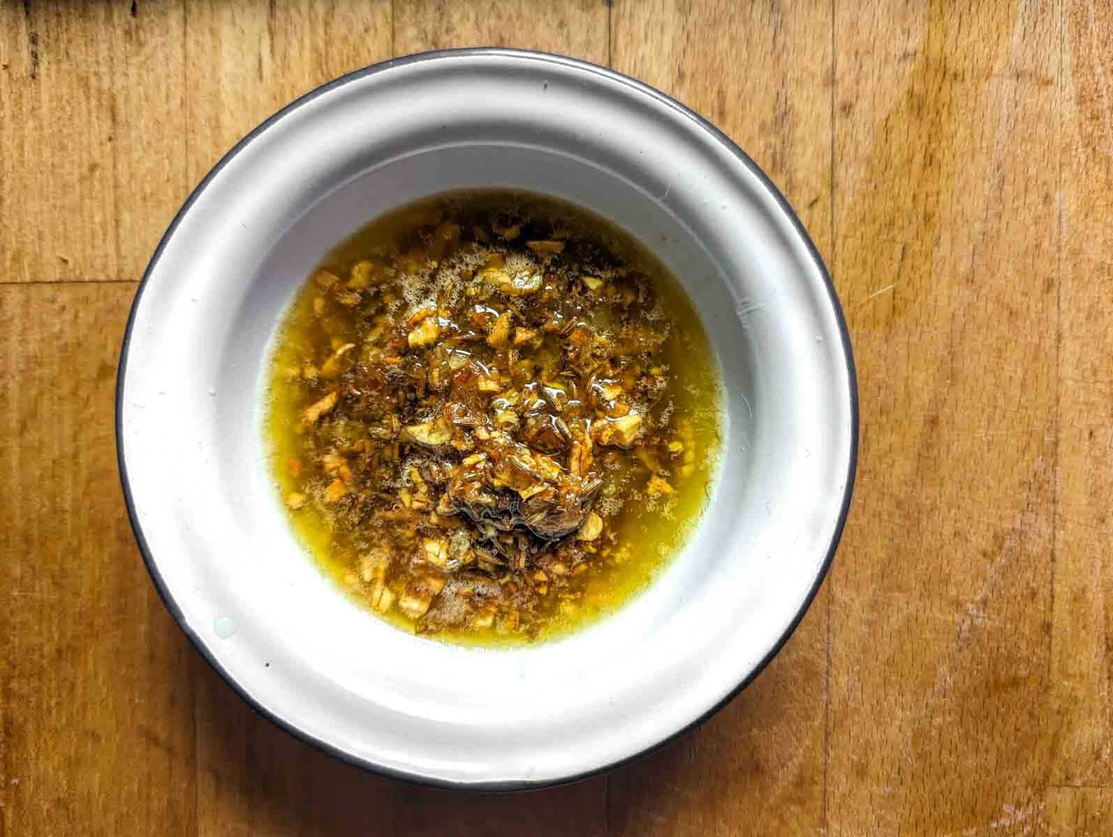 overhead shot of a small enamelware bowl with tadka of fried onion, garlic, cumin seeds, and lime juice