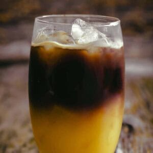 Glass filled with ice on a rustic wooden background. Bottom half of the glass is orange (because orange juice) and the top half is dark brown (coffee)
