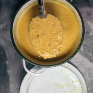 A spoon of kanom jeen nam ya curry held above a pot containing more of this textured yellow coconut curry