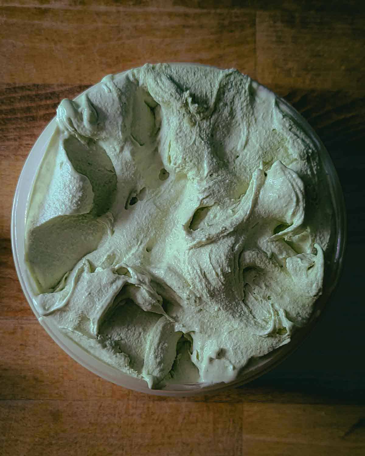 Top down view of a round plastic container filled with light green ice cream