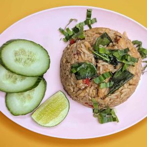 Top down view of a moulded round of fried rice topped with green herbs. There are 3 slices of cucumber and a wedge of lime next to the rice.