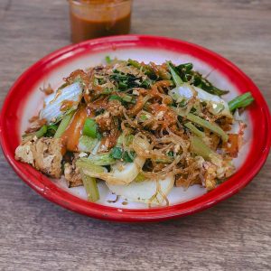 Enamelware dish with a red rim filled with noodles and green veg