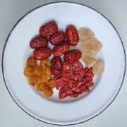 Small white plate with a blue rim filled with various dried Chinese fruits and lumps of rock sugar