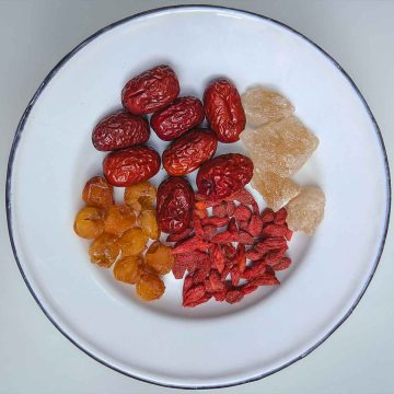 Small white plate with a blue rim filled with various dried Chinese fruits and lumps of rock sugar