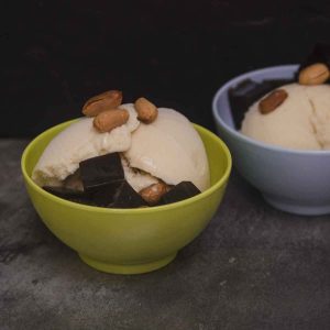 small green bowl filled with white ice cream, cubes of black jelly, and topped with peanuts