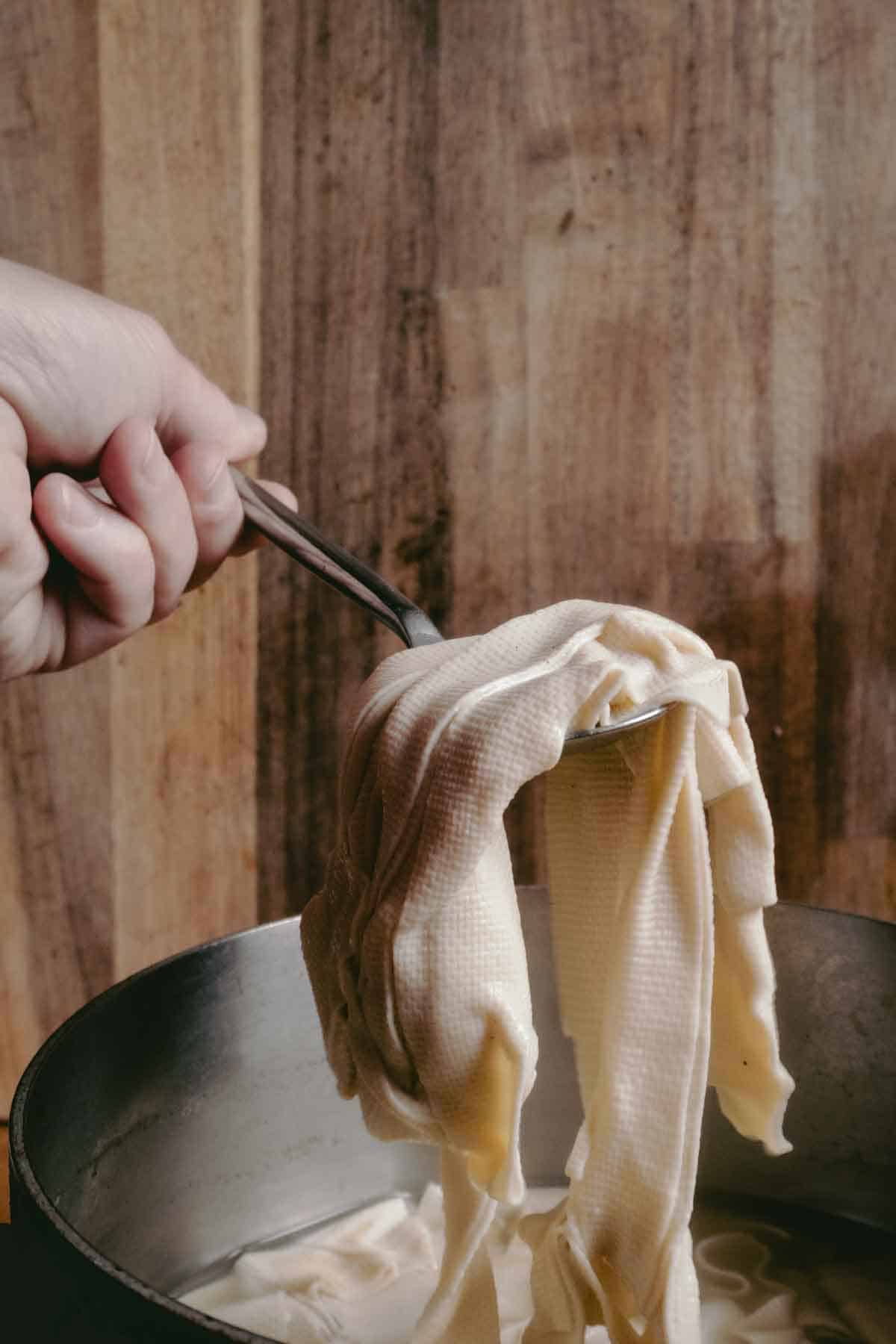 clumpy strands of thin, beige, pasta-like bits (pressed tofu sheets) stuck together, held up with a spoon out of a saucepan