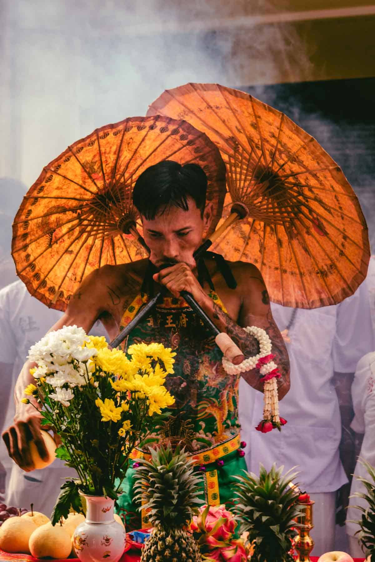 Spirit medium with two large paper umbrellas, the poles of which are piercing his cheeks