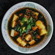 top down view of a bowl with dark broth with square yellow cubes of sweetncorn liang fen jelly