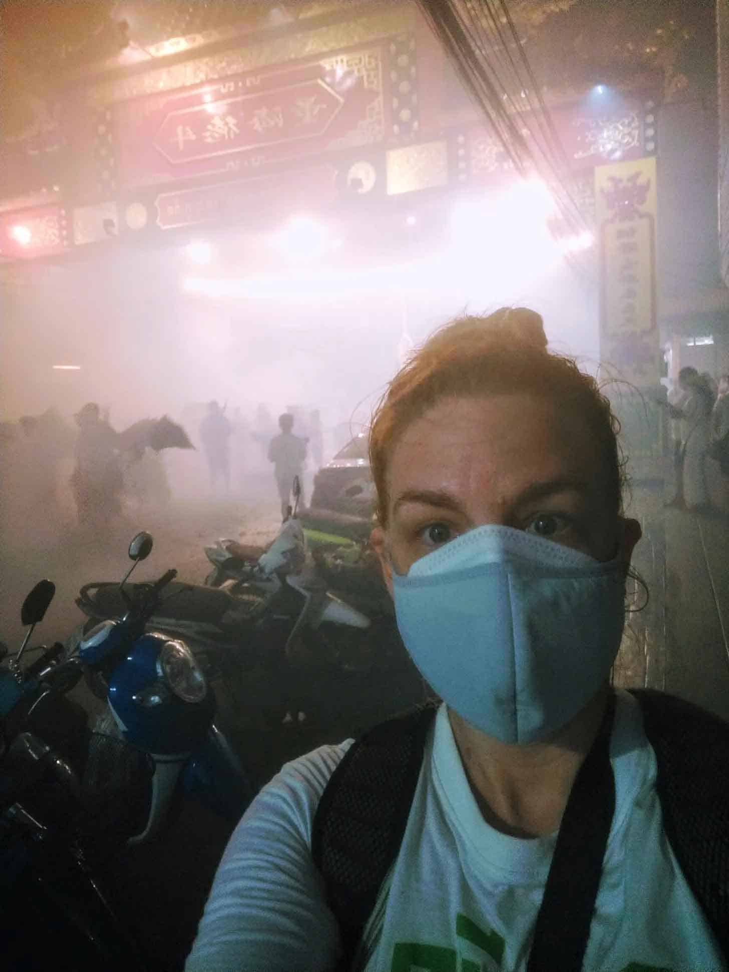 woman with two face masks on in a very smoky  (from fireworks) location at night