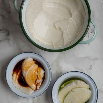 Top down view of a large pot with tofu pudding, next to two small bowls with tofu pudding.