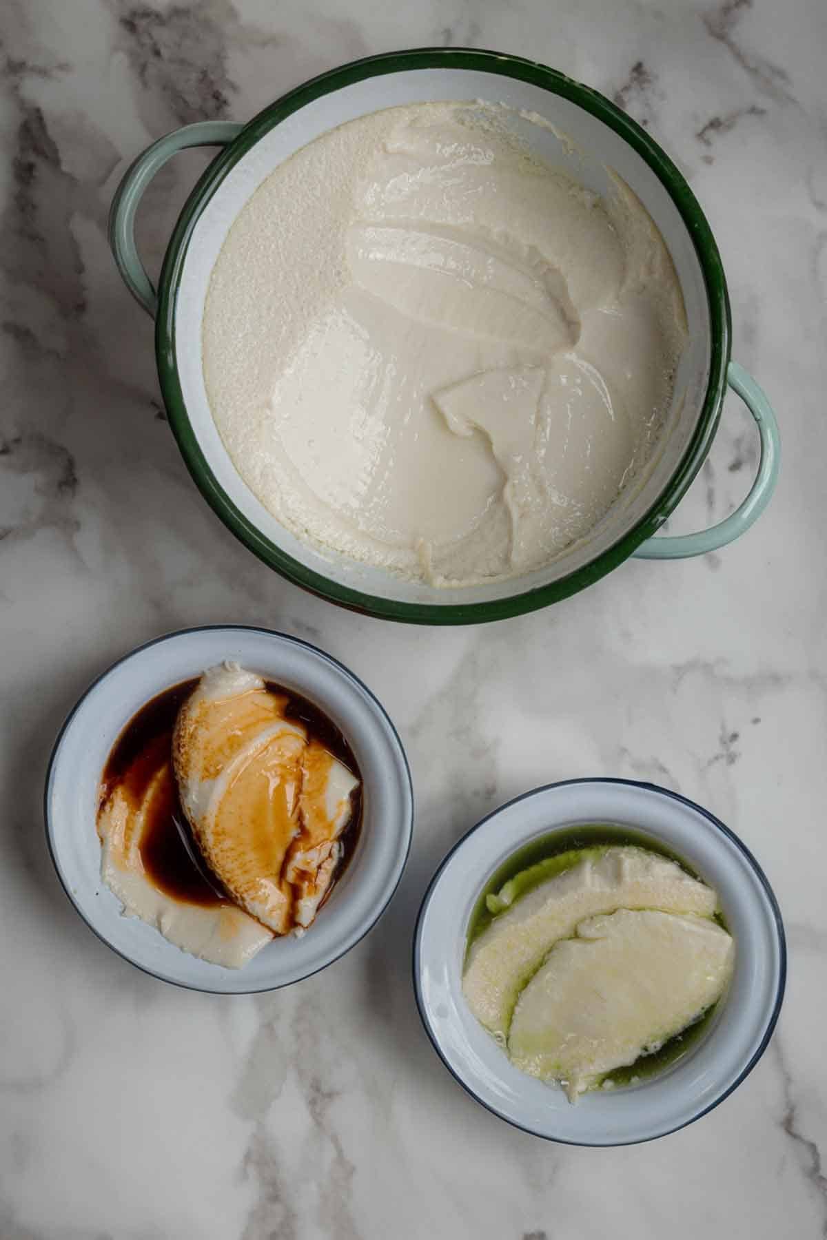 Top down view of a large pot with tofu pudding, next to two small bowls with tofu pudding.