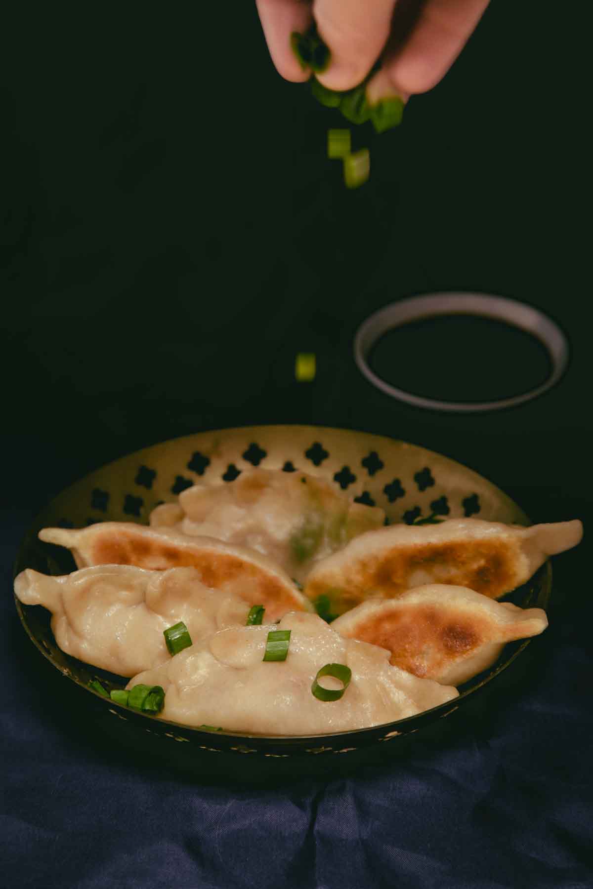 A bowl of six vegan cheeseburger dumplings with a hand sprinkling chopped spring onions over top