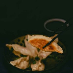 five vegan cheeseburger dumplings in a bowl. One dumpling is held up with chopsticks to showcase the crispy brown bottom.