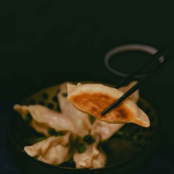 five vegan cheeseburger dumplings in a bowl. One dumpling is held up with chopsticks to showcase the crispy brown bottom.