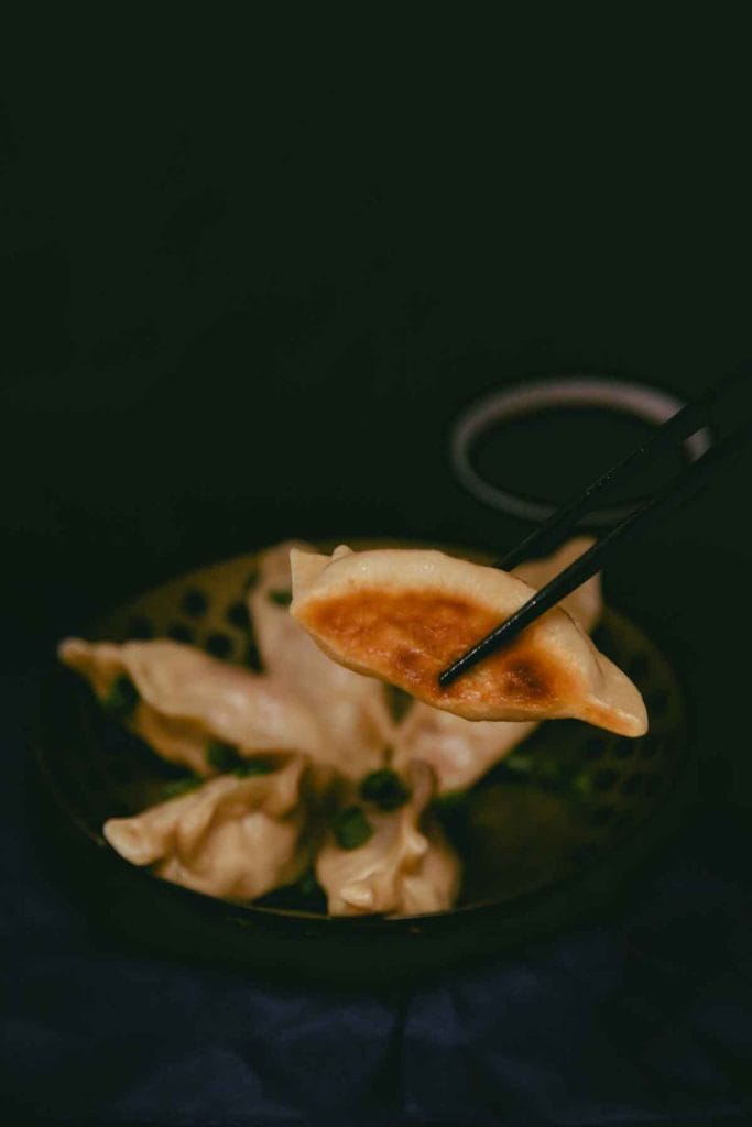 five vegan cheeseburger dumplings in a bowl. One dumpling is held up with chopsticks to showcase the crispy brown bottom.