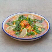 orange-yellow Passion fruit sour soup with tofu, slices of lime, and green herbs