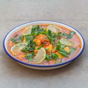 orange-yellow Passion fruit sour soup with tofu, slices of lime, and green herbs