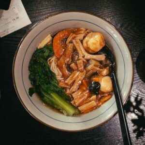 top down view of a white bowl with colourful ingredients and thin noodles