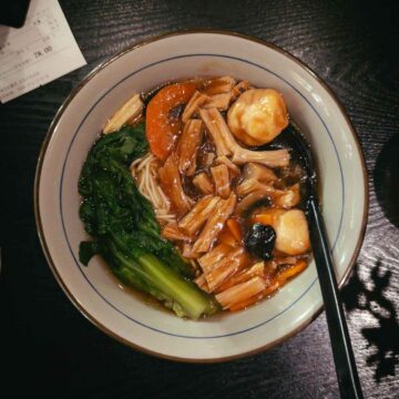 top down view of a white bowl with colourful ingredients and thin noodles